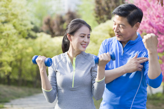 Happy mature couple exercising with dumbbell in park