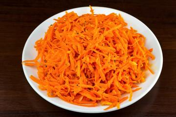 Spicy salad of grated carrots in plate on wooden background