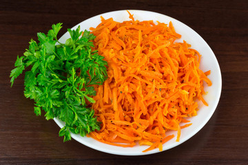 Spicy salad of grated carrots in bowl on wooden background