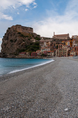 Fototapeta na wymiar Stone beach and old small italian town on cliff under blue sky