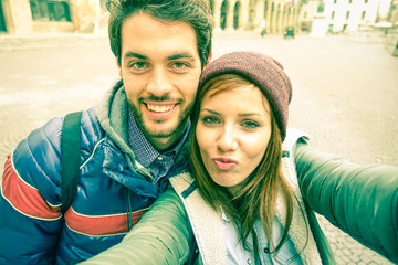 Young couple taking selfie by mobile phone in old city - Students teenager having fun with funny face expression for self photo with smartphone - Concept of joy and  memories vintage cold tones filter