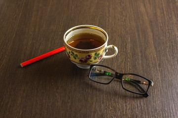 cup of tea, mobile phone,  pencil, glasses on wooden office desktop