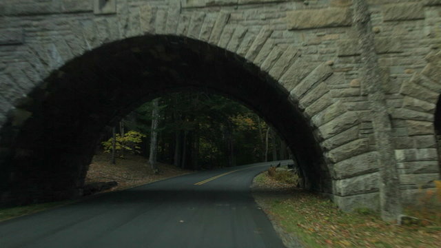 Driving on Stanley Brook Road passing under Stanley Brook Bridge with a horse-drawn carriage crossing on it, in Acadia National Park in Autumn. 
