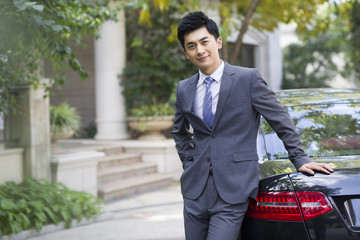 Portrait of young businessman leaning against his car