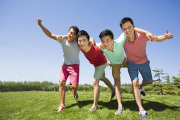 Four cheerful young men standing arm in arm on grass