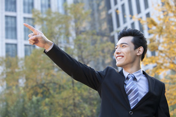 Businessman outside office buildings pointing to something