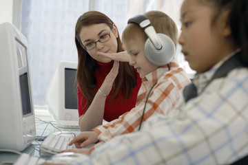 Teacher Signaling Next To Children Using Computers