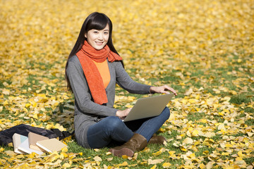 Happy young woman using laptop on the lawn in autumn