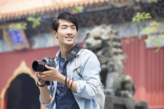 Smiling young man holding camera while standing outdoors