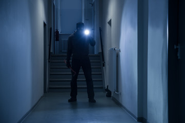 Burglar With Flashlight And Crowbar In Office Corridor