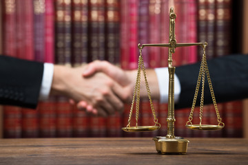 Justice Scale On Table With Judge And Client Shaking Hands