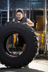 Fototapeta na wymiar Young man pushing large tire in crossfit gym