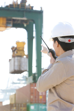 shipping industry worker directing cranes with his walkie-talkie