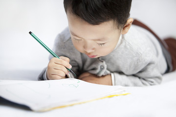 Happy little boy lying on front and writing