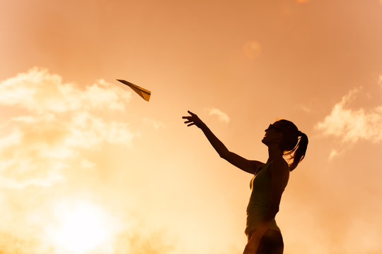 Beautiful silhouette of young woman throwing paper airplane.
