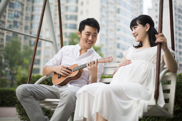 Young man playing guitar to her pregnant wife