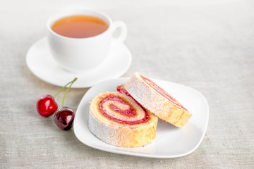 roll with berries cherry on plate and cap of tea, close up