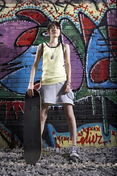 Teenage Girl With Skateboard Leaning On A Wall Of Graffiti