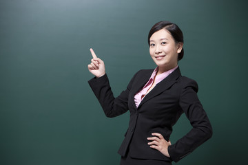 Smiling female teacher pointing to blackboard in classroom