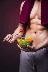 Muscular man holding a bowl of salad on grunge background
