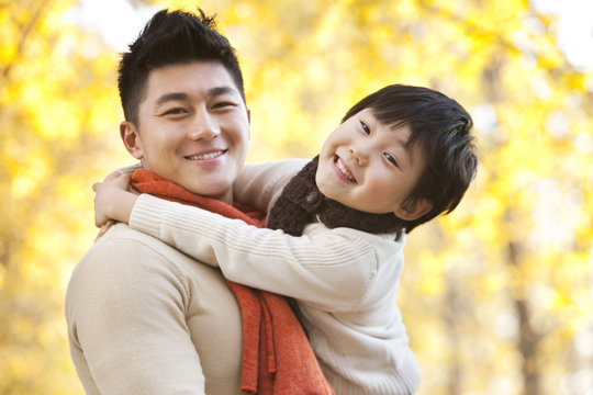 Father carrying son surrounded by Autumn trees in the background