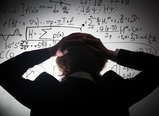 Student holding his head looking at complex math formulas on whiteboard. Problem to solve
