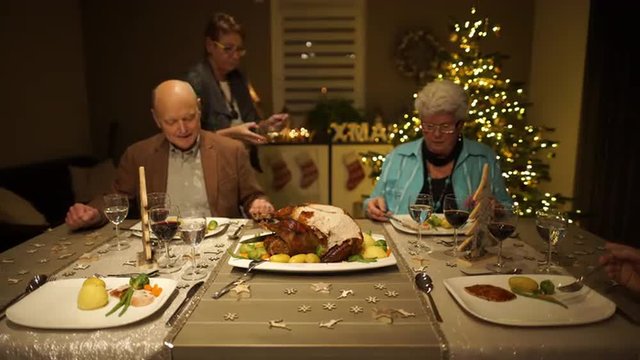 4k footage, seniors sitting on dining table at home on christmas eve with roasted turkey and woman putting jus  on plates, captured with atomos shogun
