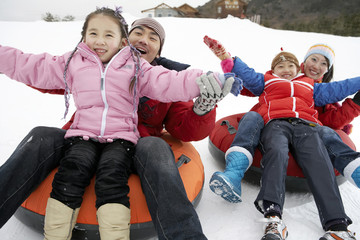 Parents And Children Riding On Inflatable Snow Tube