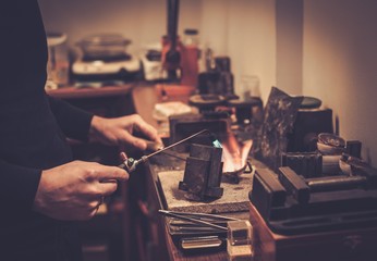 Goldsmith melting gold to liquid state in crucible with gasoline burner.