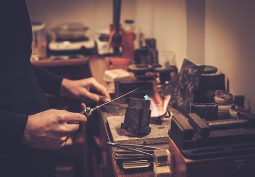 Goldsmith melting gold to liquid state in crucible with gasoline burner.
