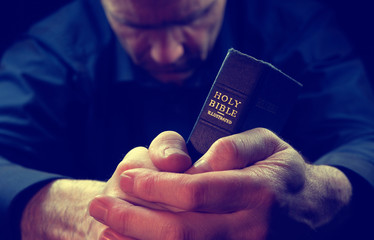 A Man praying holding a Holy Bible.