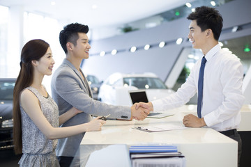 Young couple buying car in showroom