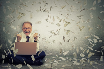 Senior man using laptop building online business making money dollar bills falling down.