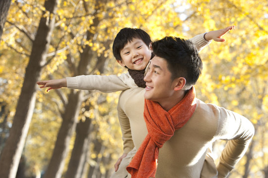 Father and son with arms outstretched and surrounded by Autumn trees