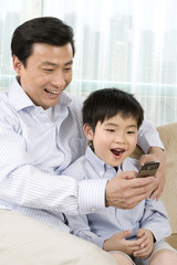 Father and son use cell phone or PDA on sofa