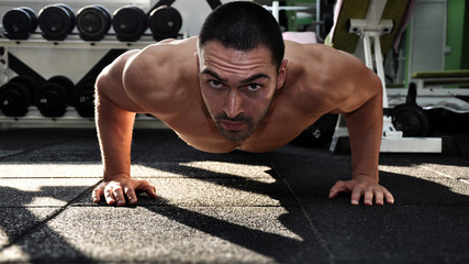 Fototapeta na wymiar Young muscular man doing push-ups on the gym . Looking at camera.