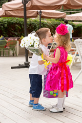 The boy kid gives flowers to girl child on birthday. Little adorable girl celebrating 3 years birthday. Childhood.