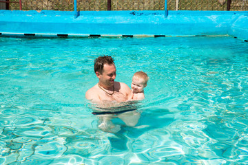 Active father teaching his child to swim in pool on tropical resort. Summer vacations and sport concept