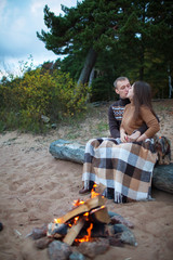 Loving couple with dog sitting on a log by the fire on the rocky beach