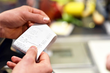 Hände mit Kassenzettel an der Kasse im Supermarkt // hands with receipt at the checkout in the...
