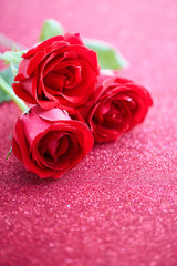 Three red roses over pink glittering background 