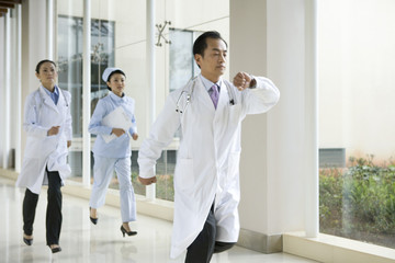 Doctors and a Nurse Run Down a Hospital Corridor