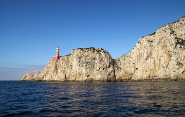 Punta Carena Lighthouse on the coastal rocks at the Mediterranean Sea in Capri island, seen from a motor boat tour.