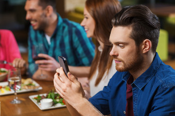 man with smartphone and friends at restaurant