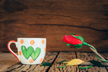 Vintage love cup with rose on old wood background.
