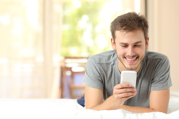 Guy using a mobile phone on a bed at home