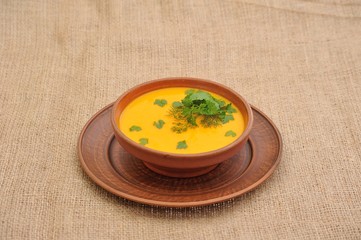 Pumpkin Soup; a bowl of pumpkin soup with bundle of greens and slices of bread