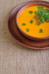 Pumpkin Soup; a bowl of pumpkin soup with bundle of greens and slices of bread