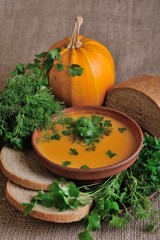 Pumpkin Soup; a bowl of pumpkin soup with bundle of greens and slices of bread