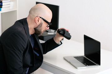 Mann blickt durch Fernglas auf Laptop